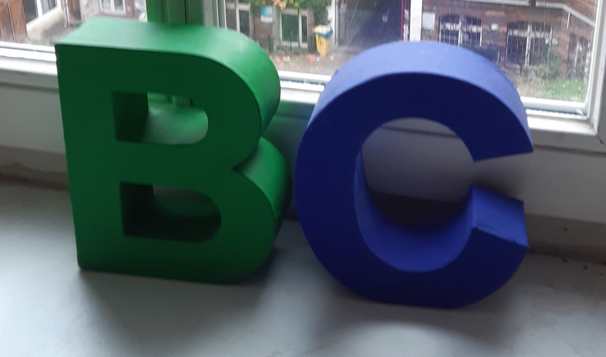 Dreidimensionale grüne und blaue Buchstaben B und C auf einer Fensterbank